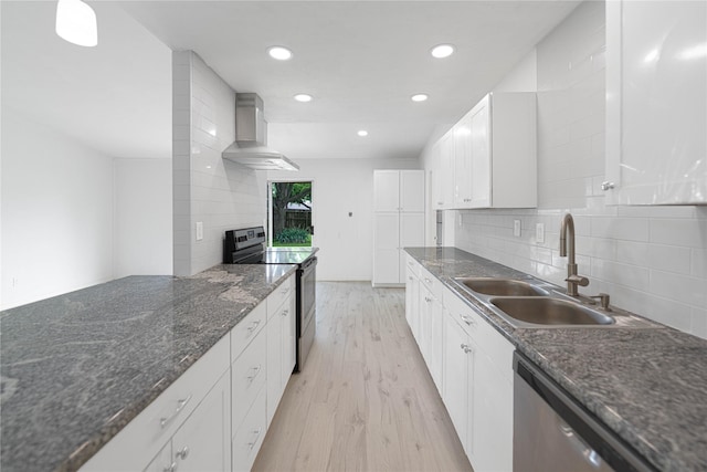 kitchen featuring a sink, wall chimney exhaust hood, backsplash, light wood-style floors, and appliances with stainless steel finishes