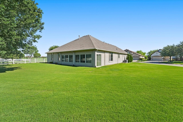 back of property with a yard, stucco siding, fence, and roof with shingles