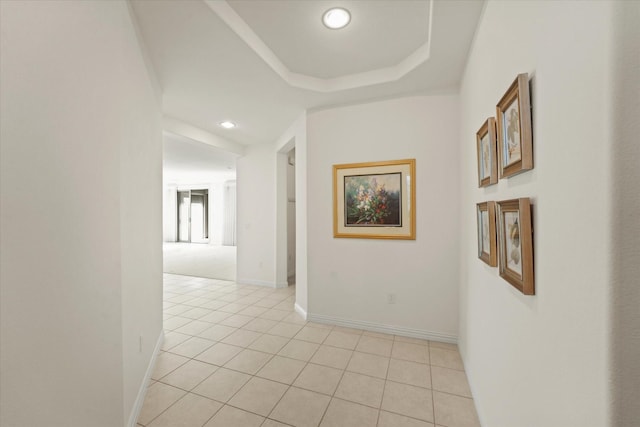 hallway with light tile patterned floors, baseboards, a raised ceiling, and recessed lighting