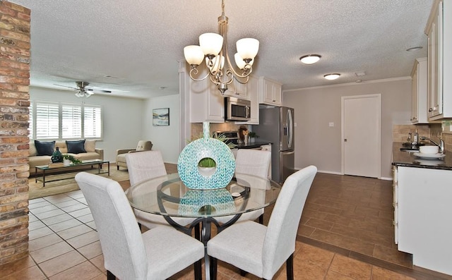 tiled dining room featuring crown molding, a textured ceiling, ceiling fan with notable chandelier, and a sink