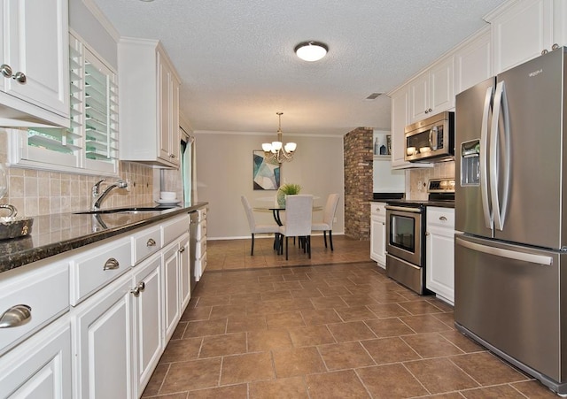kitchen featuring an inviting chandelier, a sink, stainless steel appliances, white cabinetry, and backsplash