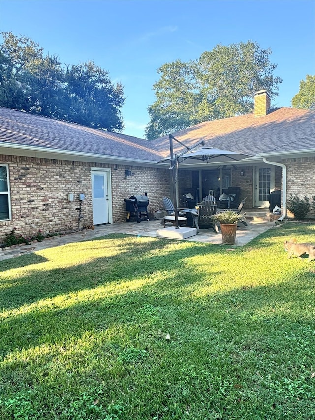 rear view of property featuring a patio area, roof with shingles, brick siding, and a lawn