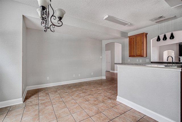 1001 Benjamin Dr, Burleson, TX 76028 - kitchen featuring light tile patterned floors, a sink, brown cabinetry, a textured ceiling, and arched walkways