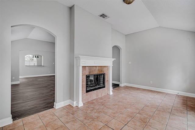 1001 Benjamin Dr, Burleson, TX 76028 - unfurnished living room featuring vaulted ceiling, a tiled fireplace, light tile patterned floors, and visible vents