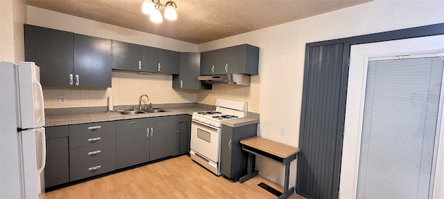 kitchen featuring light wood finished floors, a sink, white appliances, under cabinet range hood, and tasteful backsplash