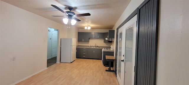 kitchen with freestanding refrigerator, a textured ceiling, light wood-style flooring, and gas range oven