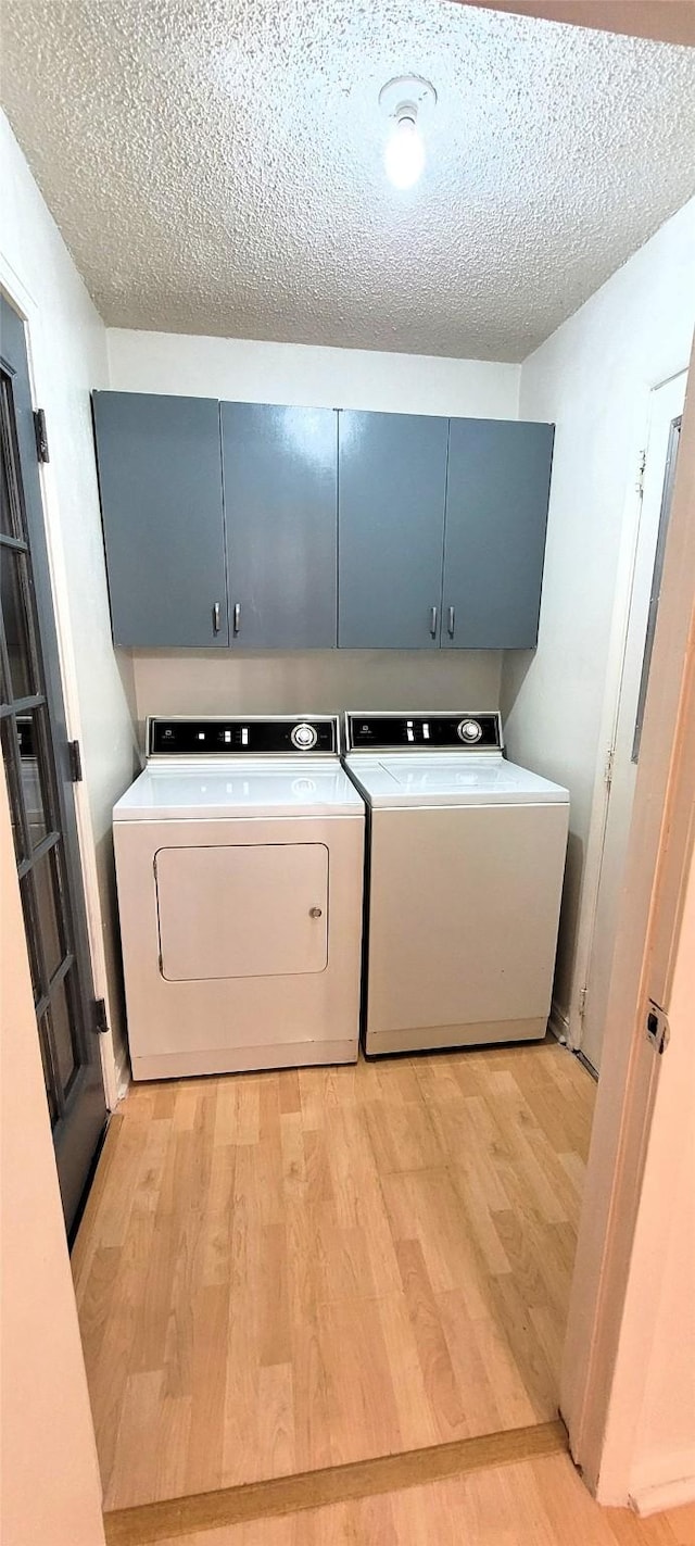 laundry area featuring washing machine and dryer, light wood finished floors, a textured ceiling, and cabinet space