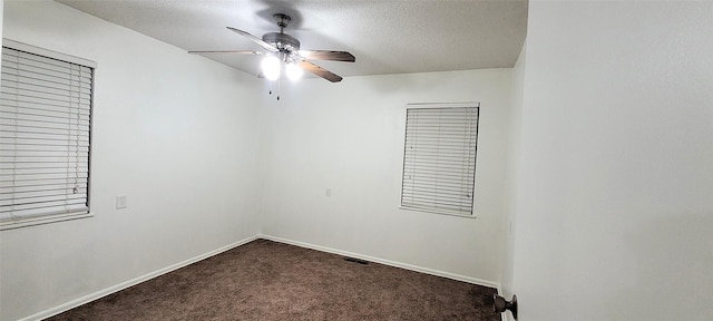 unfurnished room with a ceiling fan, baseboards, dark colored carpet, and a textured ceiling