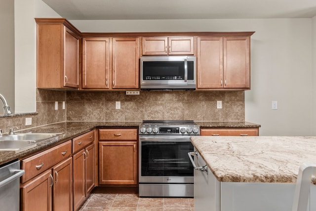 kitchen featuring a sink, stainless steel appliances, tasteful backsplash, brown cabinets, and stone counters