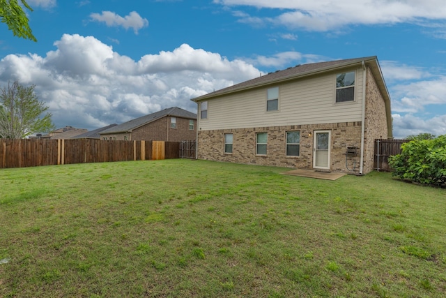 back of house with a fenced backyard, brick siding, and a lawn