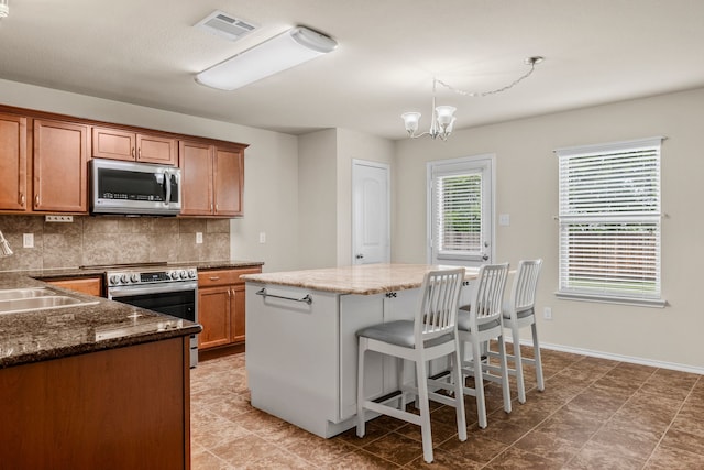 kitchen with brown cabinetry, visible vents, a chandelier, decorative backsplash, and appliances with stainless steel finishes