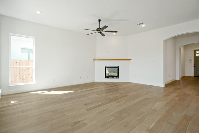 629 Hummingbird Dr, Aledo, TX 76008 - unfurnished living room featuring visible vents, light wood finished floors, arched walkways, a ceiling fan, and a glass covered fireplace