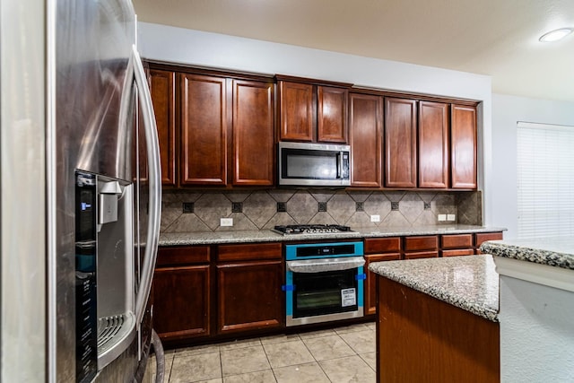 kitchen featuring light tile patterned floors, stainless steel appliances, light stone counters, and backsplash