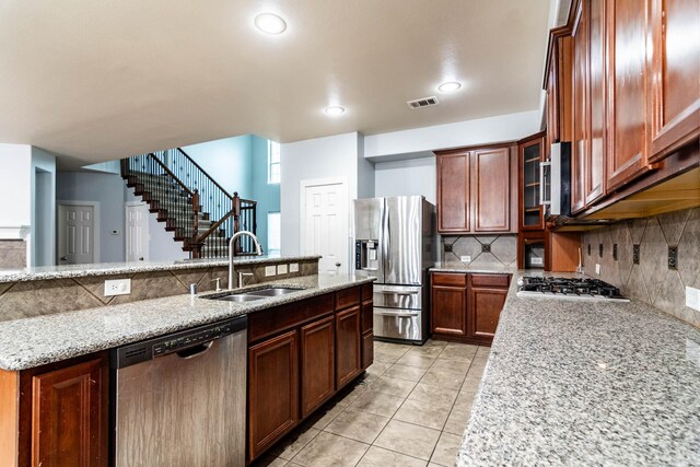 kitchen featuring appliances with stainless steel finishes, a sink, tasteful backsplash, light stone countertops, and light tile patterned floors