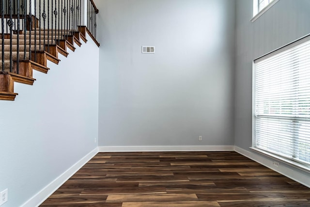 unfurnished room featuring baseboards, dark wood-type flooring, and stairway