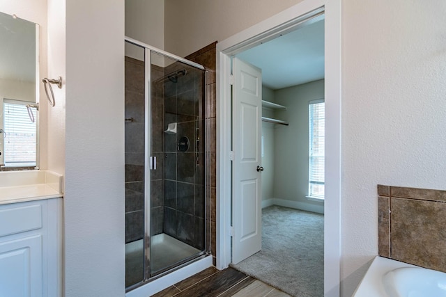 full bathroom with a stall shower, vanity, a bath, and wood finished floors