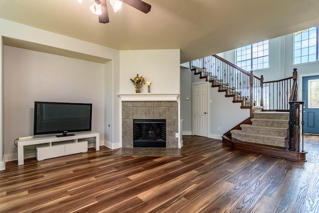 unfurnished living room featuring stairs, wood finished floors, ceiling fan, baseboards, and a fireplace