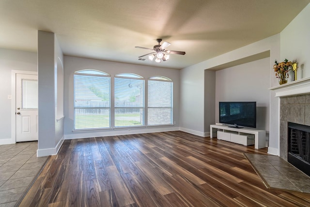 unfurnished living room with a ceiling fan, baseboards, a tile fireplace, and wood finished floors