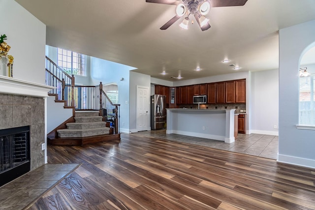 unfurnished living room with dark wood-style floors, stairs, a ceiling fan, and a tiled fireplace