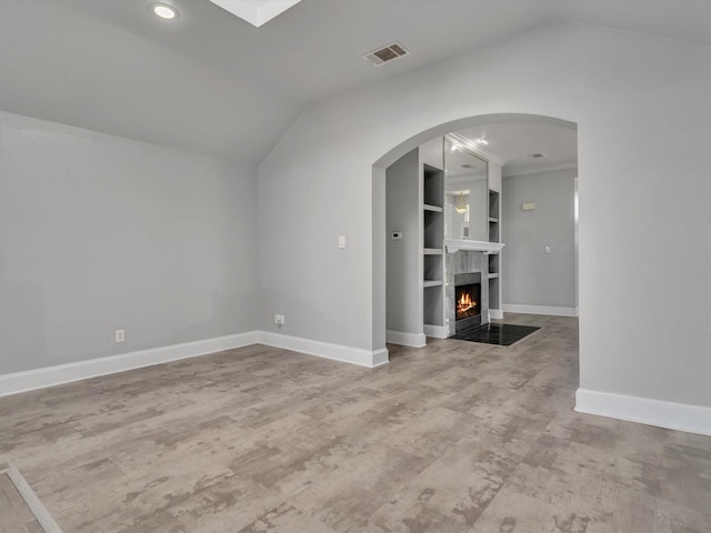 unfurnished living room featuring vaulted ceiling, baseboards, a fireplace with flush hearth, wood finished floors, and arched walkways