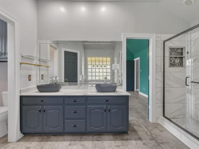 bathroom featuring toilet, a marble finish shower, double vanity, and lofted ceiling