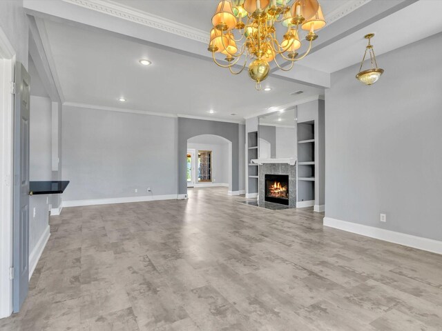 unfurnished living room featuring a chandelier, arched walkways, ornamental molding, built in features, and baseboards