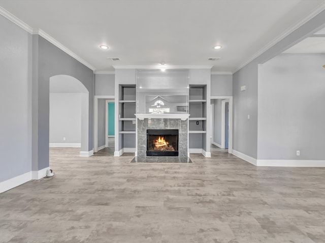 unfurnished living room featuring baseboards, a tiled fireplace, ornamental molding, arched walkways, and built in features