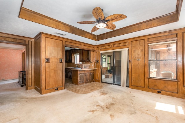107 Russell Dr, Highland Village, TX 75077 - kitchen featuring a raised ceiling, light colored carpet, a ceiling fan, brown cabinets, and wood walls