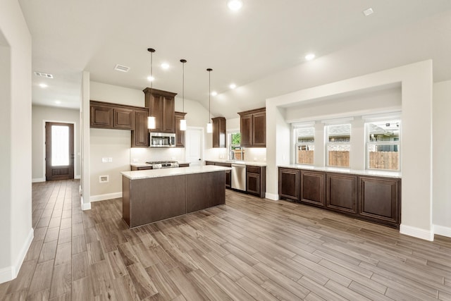 kitchen with stainless steel appliances, light countertops, light wood-type flooring, a kitchen island, and lofted ceiling