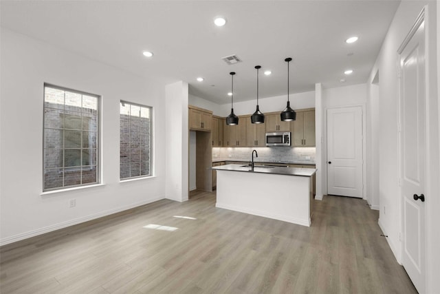2418 Bulin, Mansfield, TX 76063 - kitchen with stainless steel microwave, a sink, a kitchen island with sink, light wood finished floors, and decorative backsplash