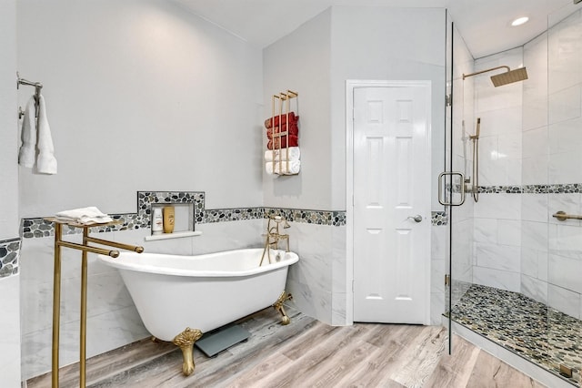 full bathroom featuring tile walls, wood finished floors, a stall shower, wainscoting, and a freestanding tub