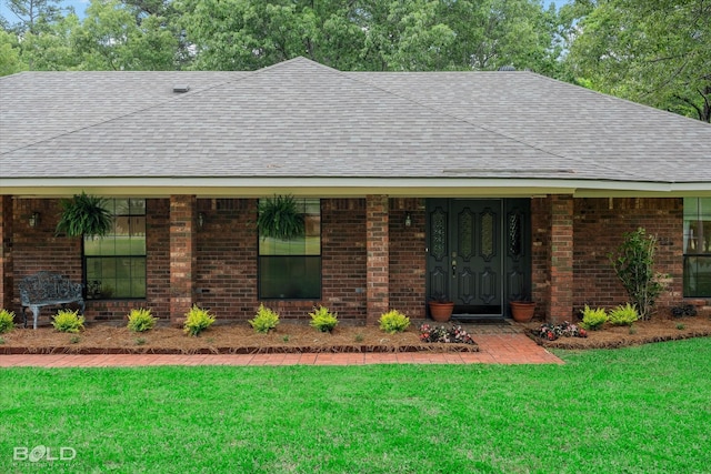 view of front of house featuring brick siding, roof with shingles, and a front yard