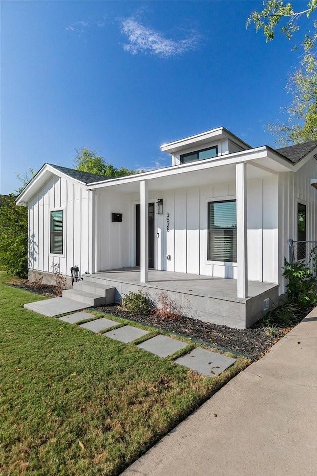 view of front facade with board and batten siding, a porch, and a front lawn