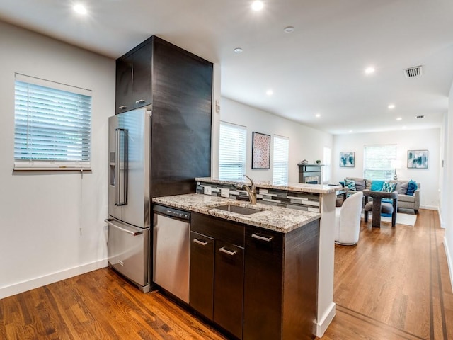 kitchen featuring a peninsula, wood finished floors, a sink, appliances with stainless steel finishes, and light stone counters