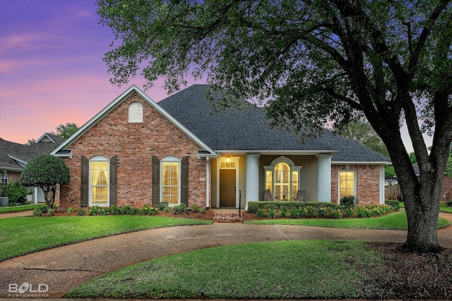 view of front of house with a yard, brick siding, and a shingled roof