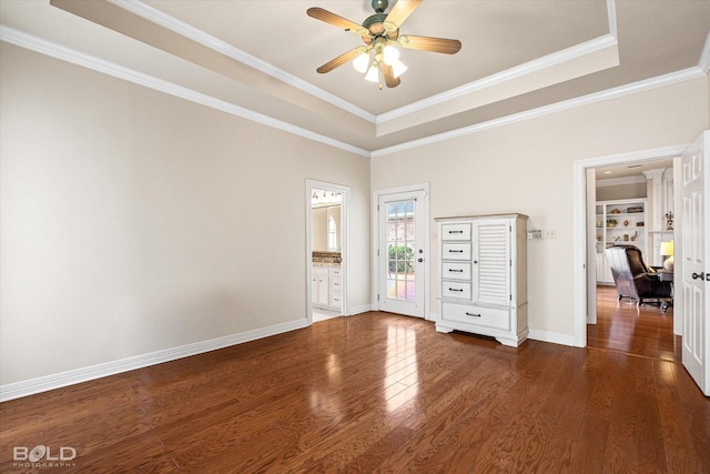 empty room with wood finished floors, a ceiling fan, a tray ceiling, crown molding, and baseboards