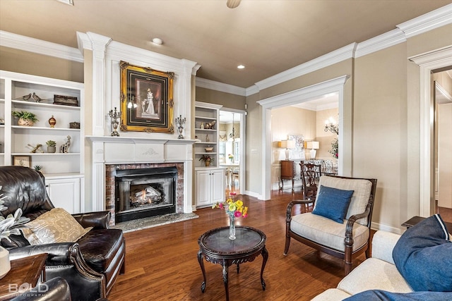 living area with crown molding, baseboards, dark wood-style floors, built in shelves, and a warm lit fireplace