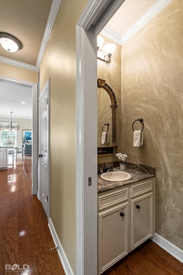 bathroom with wood finished floors, baseboards, a chandelier, vanity, and ornamental molding