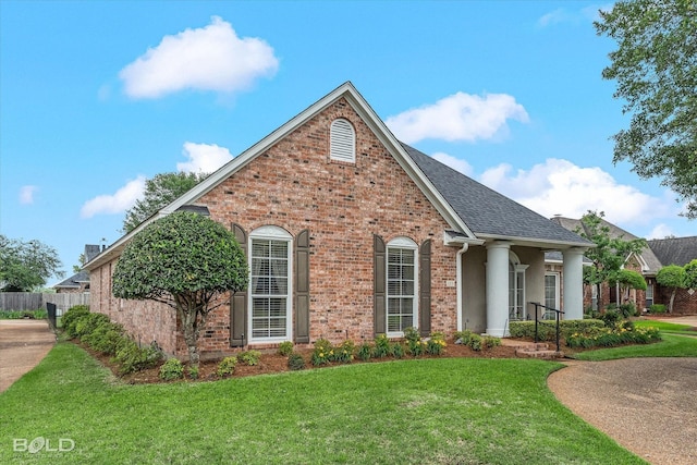 view of front of house with a shingled roof, brick siding, a front lawn, and fence