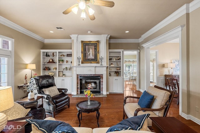 living area with wood finished floors, visible vents, crown molding, a brick fireplace, and a ceiling fan