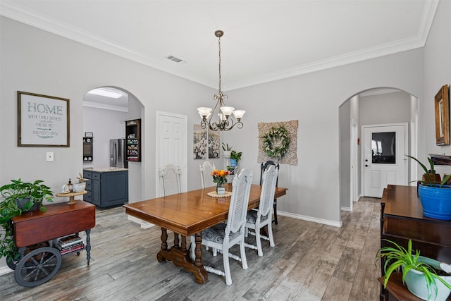 dining room featuring light wood finished floors, ornamental molding, arched walkways, and visible vents