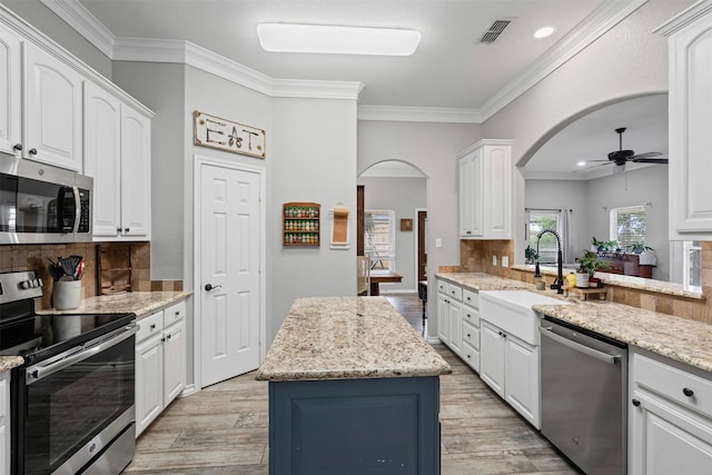 kitchen with a ceiling fan, stainless steel appliances, light wood-type flooring, visible vents, and arched walkways