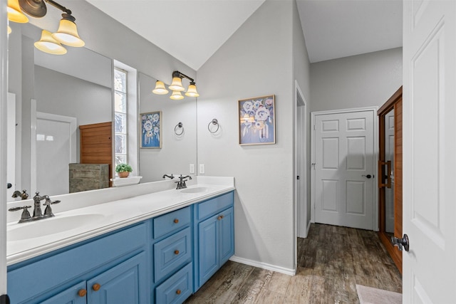 full bath with double vanity, vaulted ceiling, wood finished floors, and a sink