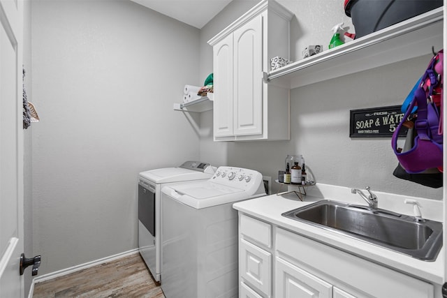 washroom with a sink, cabinet space, separate washer and dryer, light wood-style flooring, and baseboards