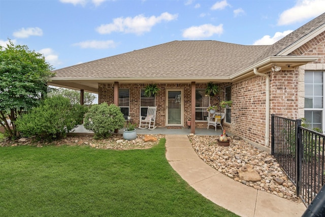 view of exterior entry with a lawn, roof with shingles, and brick siding