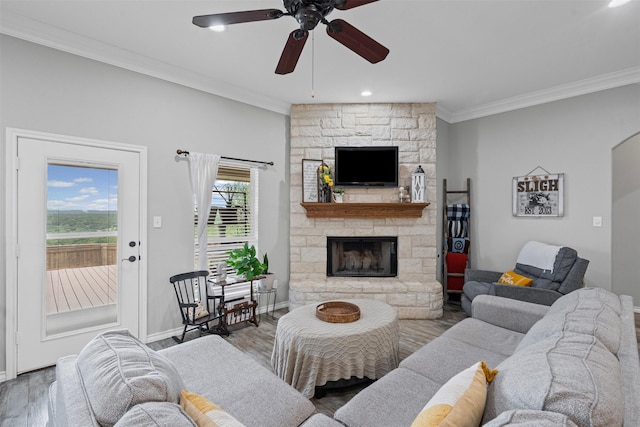 living area featuring baseboards, a stone fireplace, ornamental molding, ceiling fan, and wood finished floors