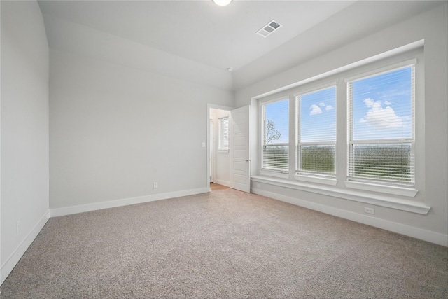 empty room featuring baseboards, lofted ceiling, visible vents, and light colored carpet