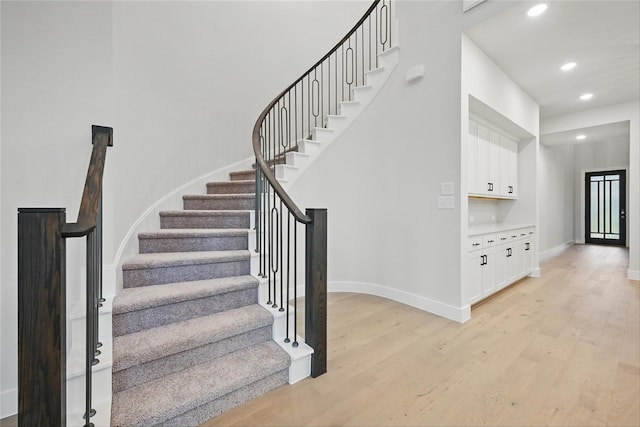 staircase featuring wood finished floors, baseboards, and recessed lighting