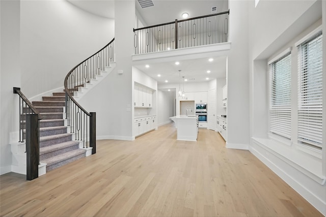 unfurnished living room featuring a towering ceiling, recessed lighting, stairway, light wood finished floors, and baseboards
