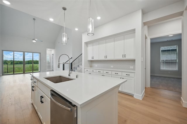 kitchen featuring a sink, light wood-style flooring, light countertops, stainless steel dishwasher, and hanging light fixtures